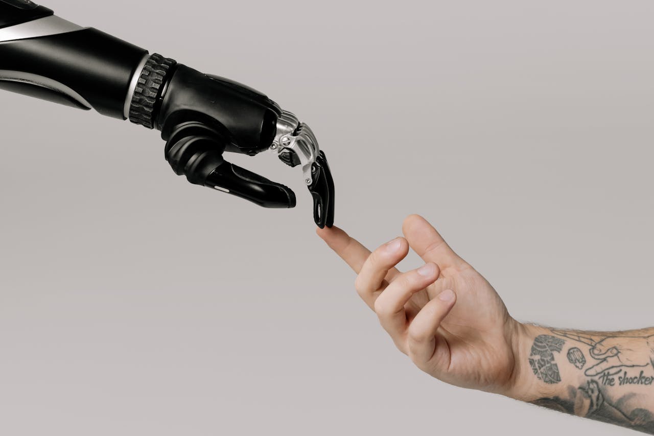 about-03 A human hand with tattoos reaching out to a robotic hand on a white background.