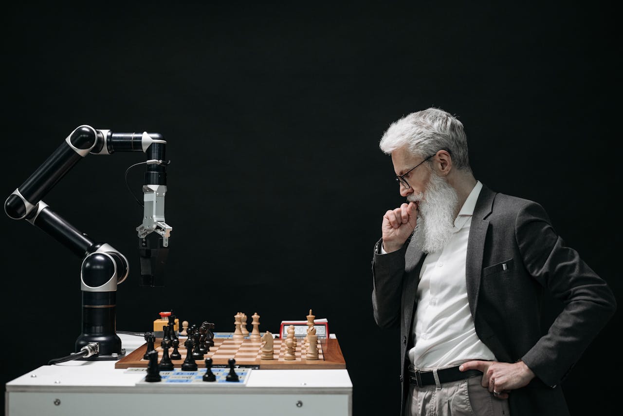 menu-01 An elderly scientist contemplates a chess move against a robotic arm on a chessboard.